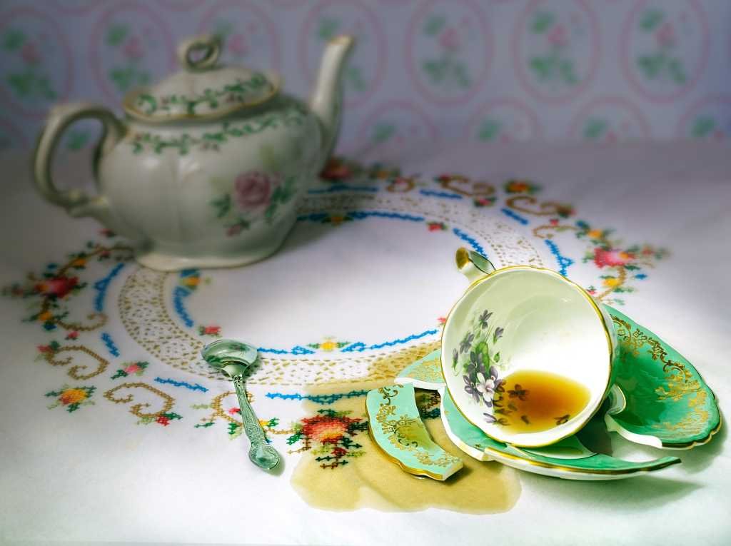 dropped  china cup of tea on a broken saucer with spilled tea on table cloth